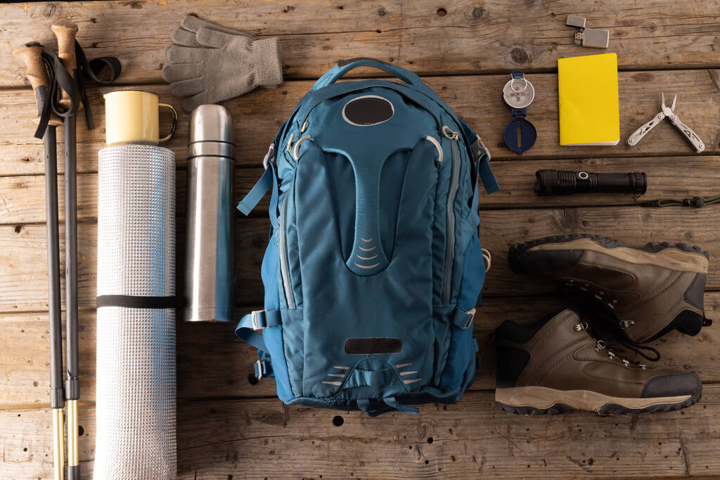 Camping equipment of backpack, mat, thermos and trekking sticks on wooden background. National camping month, equipment and celebration concept. - Photo, Image