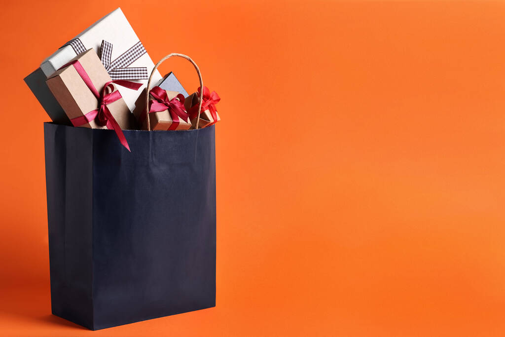 Tummansininen paperi ostoskassi täynnä lahjapakkauksia oranssi tausta. Tekstitila - Valokuva, kuva