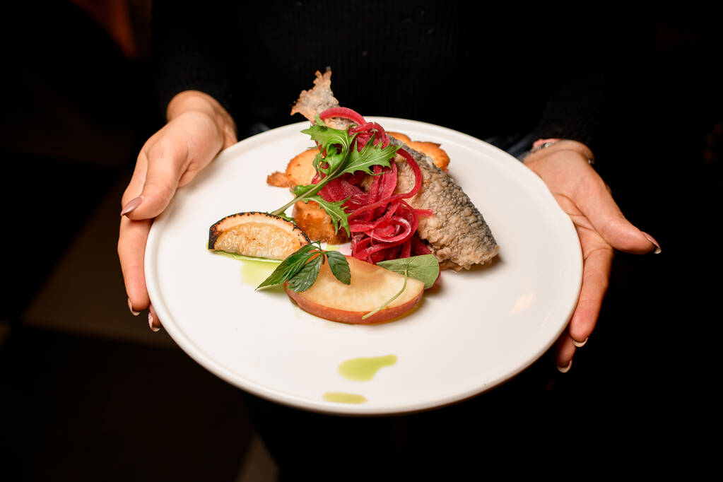тарілка зі смачною смаженою смаженою рибою, прикрашеною цибулею та лимоном та підсмаженими хлібними тостами у жіночих руках
 - Фото, зображення