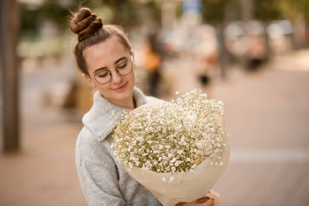 attractive young woman with large bouquet of white gypsophila flowers in wrapping paper in the hands - Photo, Image