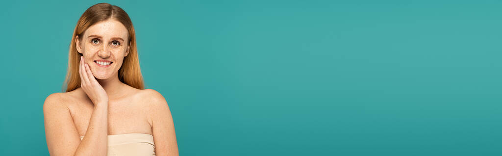 Positive young woman with freckles standing isolated on turquoise, banner  - Photo, Image