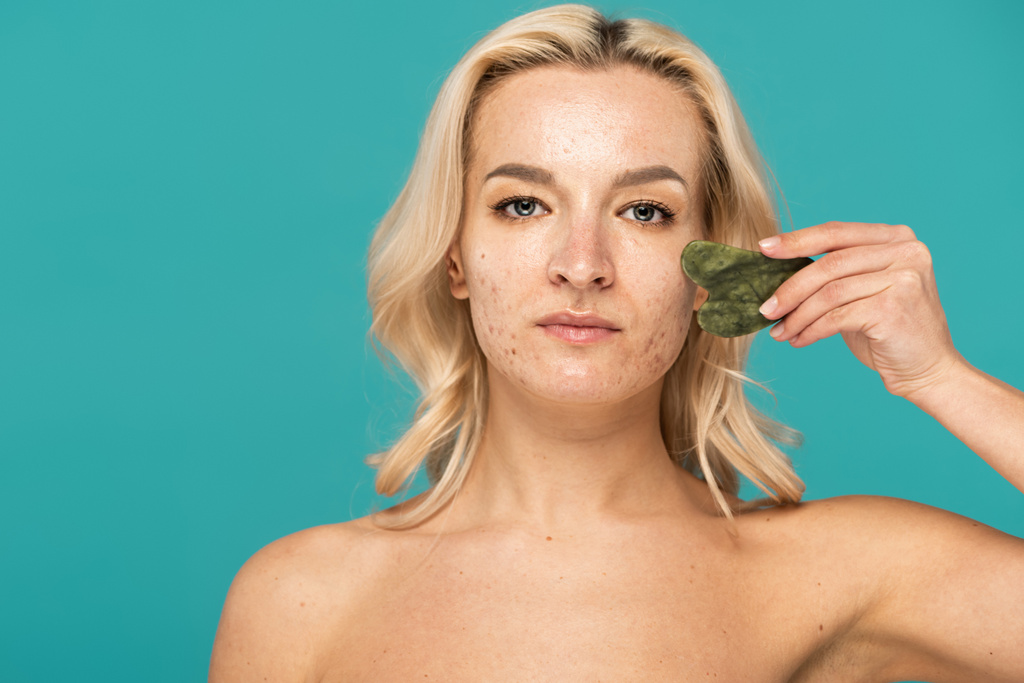 blondynka kobieta z dorosłych trądzik masowanie twarzy z jadeitowy skrobak twarzy izolowane na turkusowy - Zdjęcie, obraz