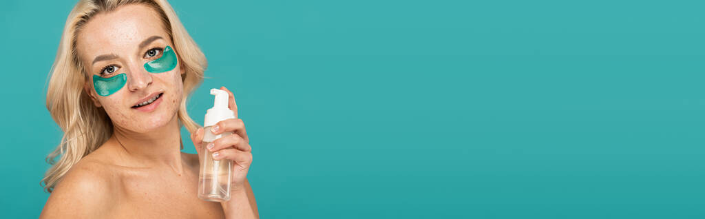 блондинка с прыщами и повязками на глазу держа бутылку с пенопластом изолирован на бирюзовый, баннер  - Фото, изображение