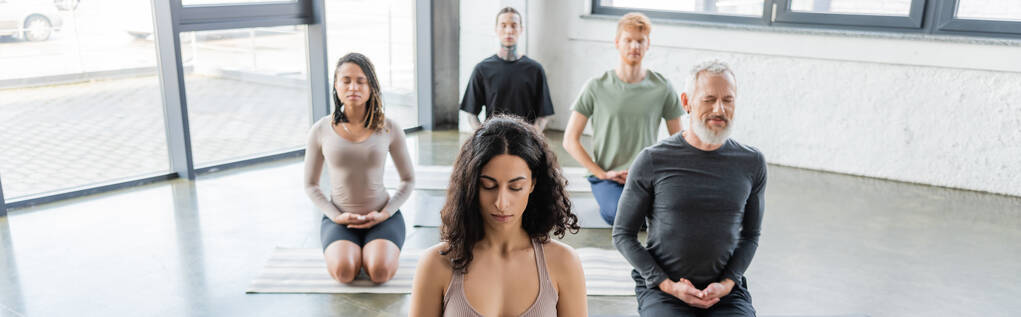 Multikulturelle Menschen meditieren im Thunderbolt Asana auf Yogamatten im Studio, Banner  - Foto, Bild