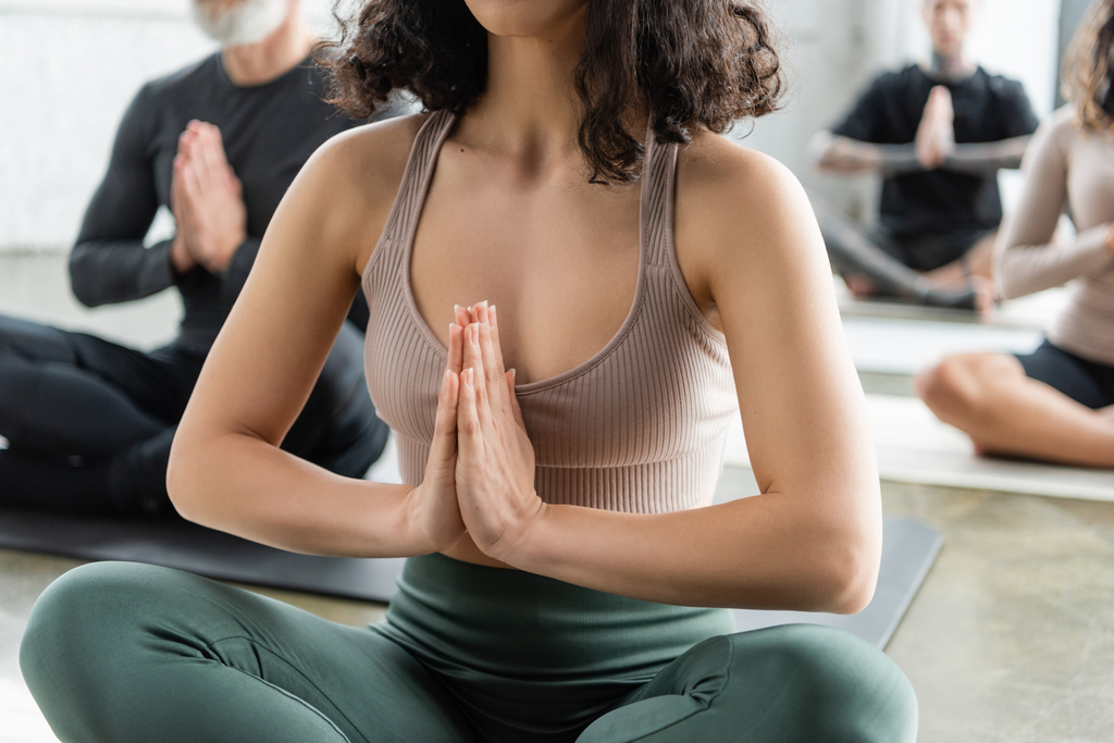 Vue recadrée de la femme en vêtements de sport méditant en cours de yoga flou  - Photo, image