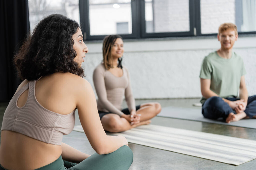 Donna mediorientale che parla con gruppo sfocato su stuoie in classe di yoga  - Foto, immagini