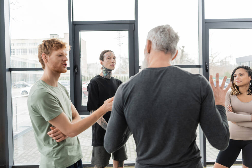 roodharige man in gesprek met wazig volwassen coach in yoga studio  - Foto, afbeelding