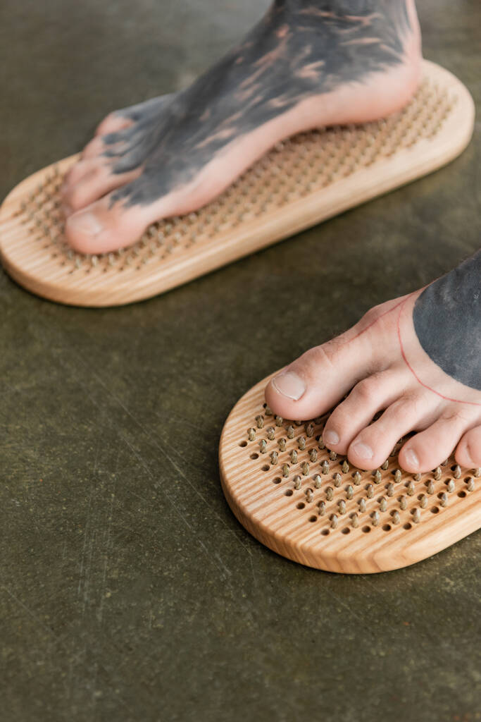 close up view of barefoot man with tattooed legs standing on sadhu nail board  - Photo, Image