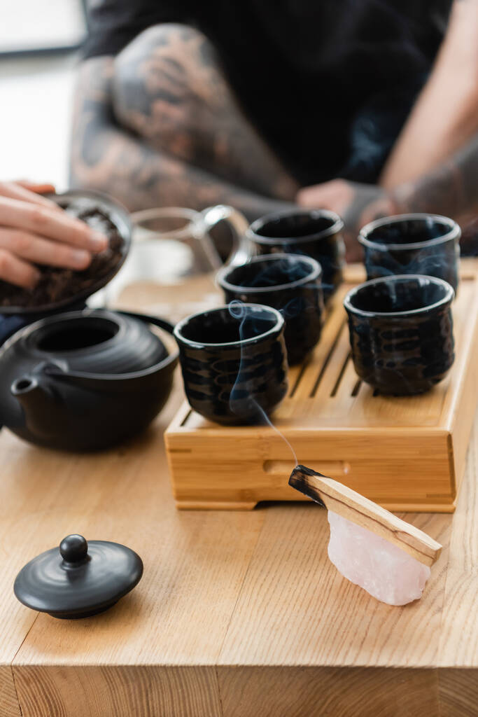 горящий Пало Санто придерживаться рядом с человеком добавив чистейший чай в традиционном китайском чайник в студии йоги  - Фото, изображение