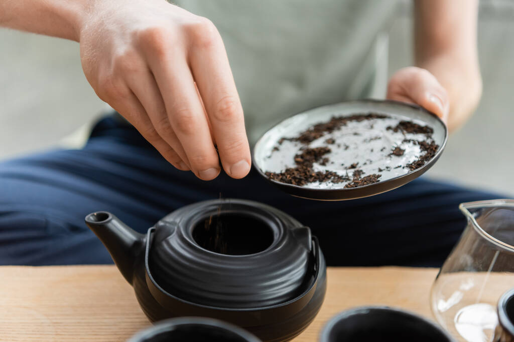 vista recortada del hombre añadiendo hojas de té secas en maceta de té chino  - Foto, imagen