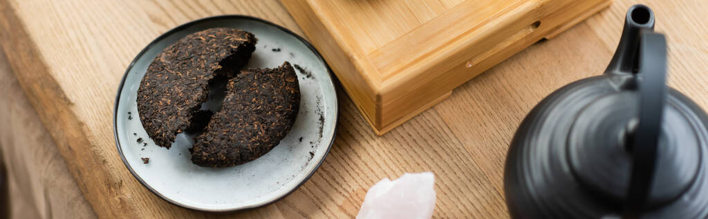 κορυφαία άποψη του συμπιεσμένου pu-erh τσάι στο πιάτο κοντά ιαπωνική τσαγιέρα στο στούντιο γιόγκα, πανό  - Φωτογραφία, εικόνα