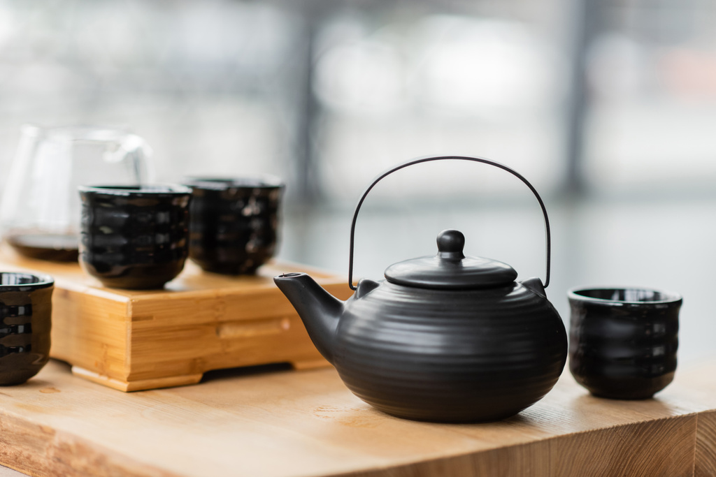 Традиційний китайський чайник біля чашок і скляного глечика з чистим чаєм на розмитому фоні.  - Фото, зображення