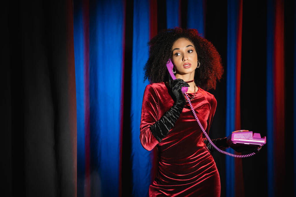 エレガントなアフリカ系アメリカ人女性でベルベットドレストーク上のレトロ電話上の青の背景に光 - 写真・画像