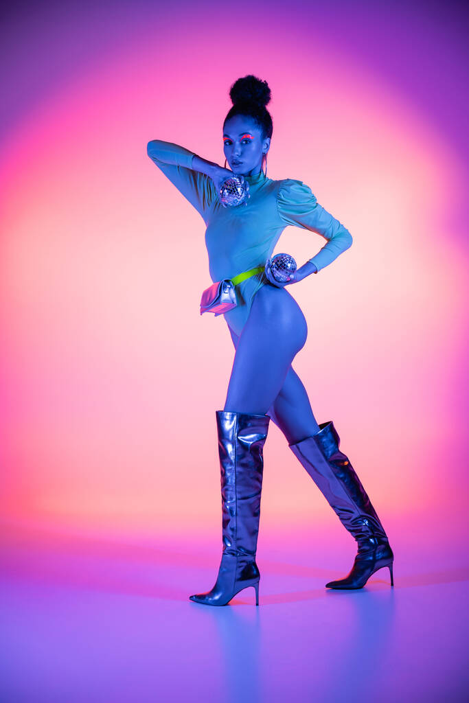 Comprimento total do moderno modelo afro-americano com visagem de néon segurando bolas de discoteca no fundo rosa e roxo - Foto, Imagem