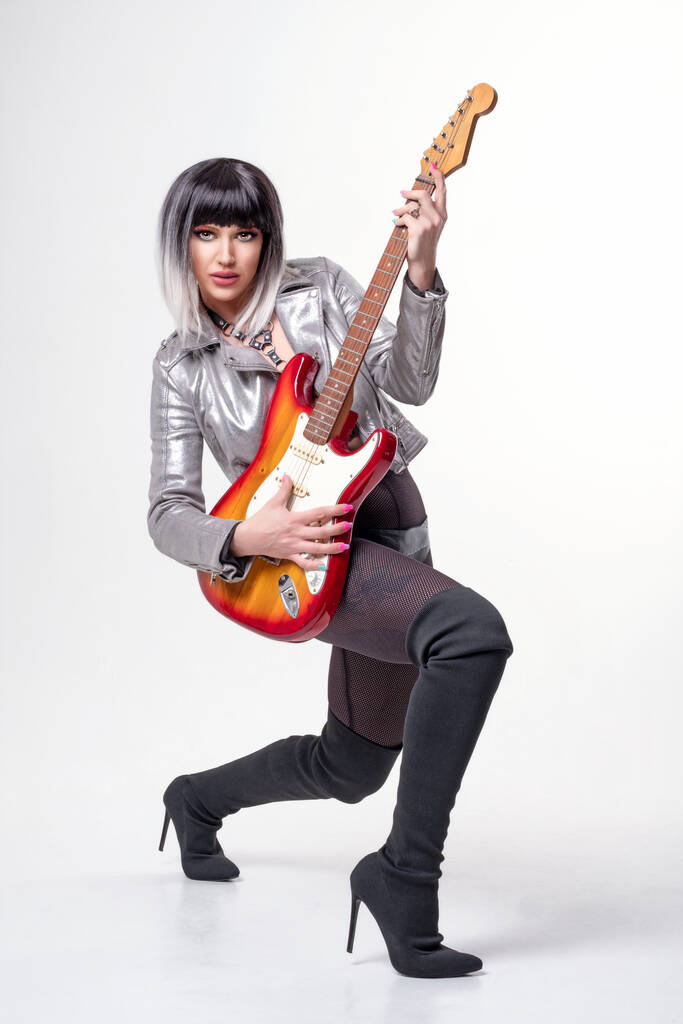 Bella donna in sexy vestito funky e stivali che tengono la chitarra elettrica su sfondo bianco - Foto, immagini