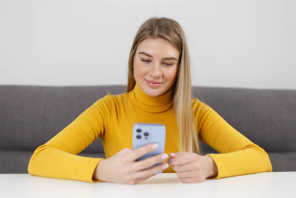 Счастливая блондинка просматривает мобильное приложение на современном синем смартфоне. Веселая украинская девушка, использующая сотовый телефон для связи - Фото, изображение
