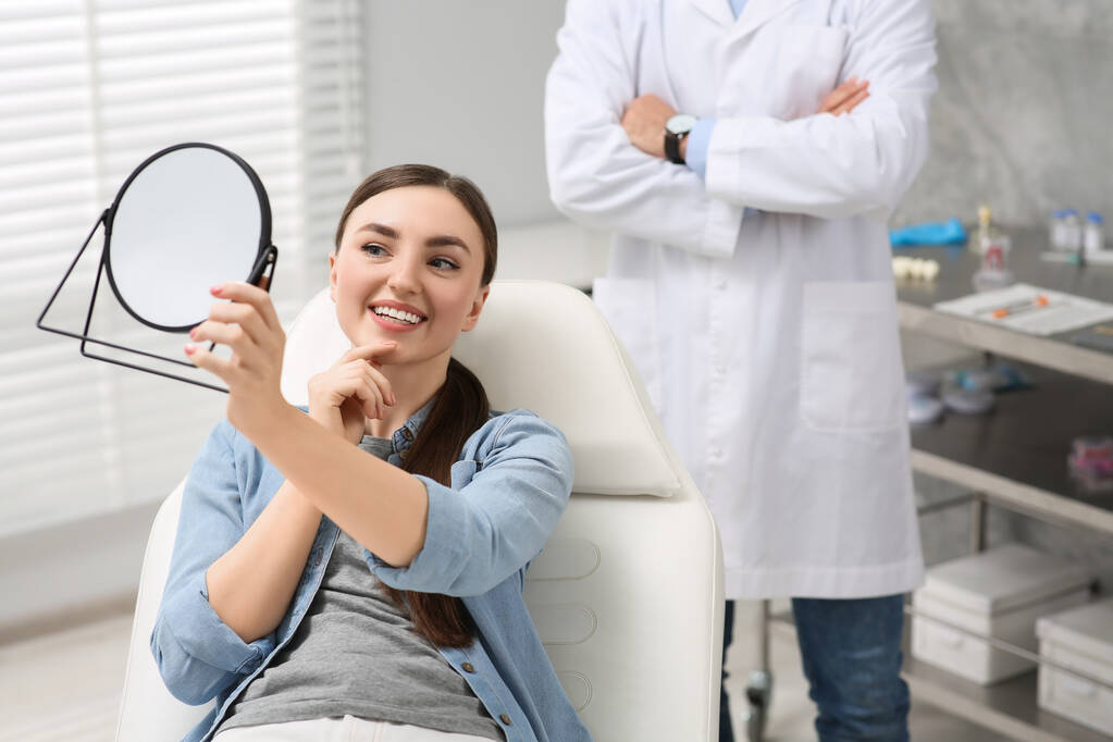 Mladá žena při pohledu na její nové zubní implantáty v zrcadle uvnitř - Fotografie, Obrázek