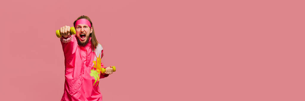Porträt eines jungen Mannes im hellen Sportbekleidungstraining mit Kurzhanteln vor rosa Studiohintergrund. Fitness. Konzept von Emotionen, Mimik, Lebensstil. Banner. Kopierraum für Werbung - Foto, Bild