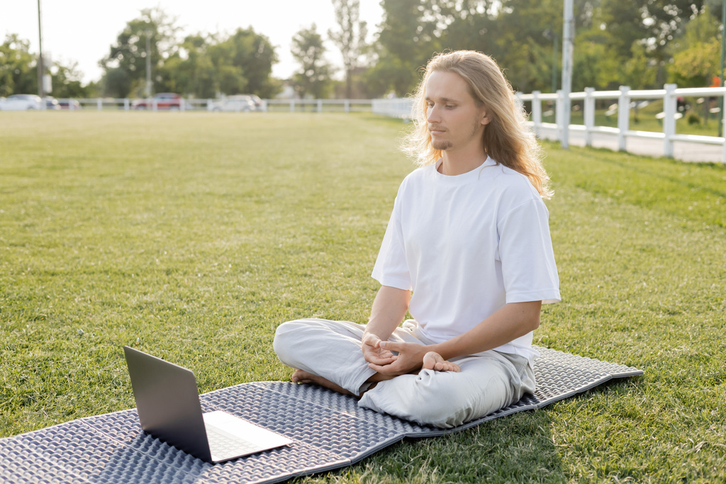 jovem meditando em pose fácil perto de laptop no tapete de ioga  - Foto, Imagem