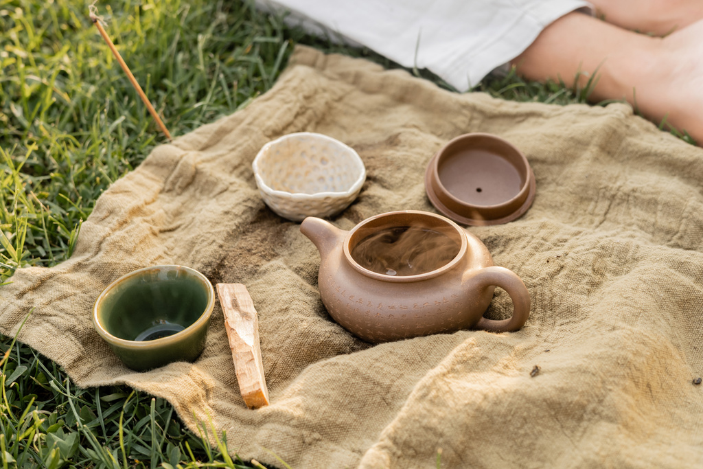 aromatic palo santo stick and ceramic teapot with cups near cropped yoga man sitting on grassy lawn - Photo, Image
