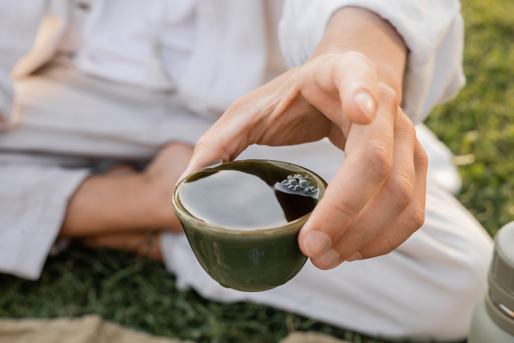 close up view of clay cup with puer tea in hand of cropped yoga man sitting outdoors - Photo, Image