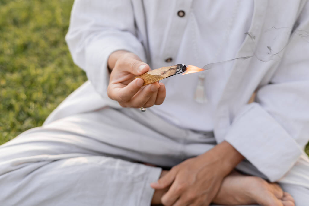 partial view of man in white cotton clothes holding burning palo santo stick while meditating outdoors - Photo, Image