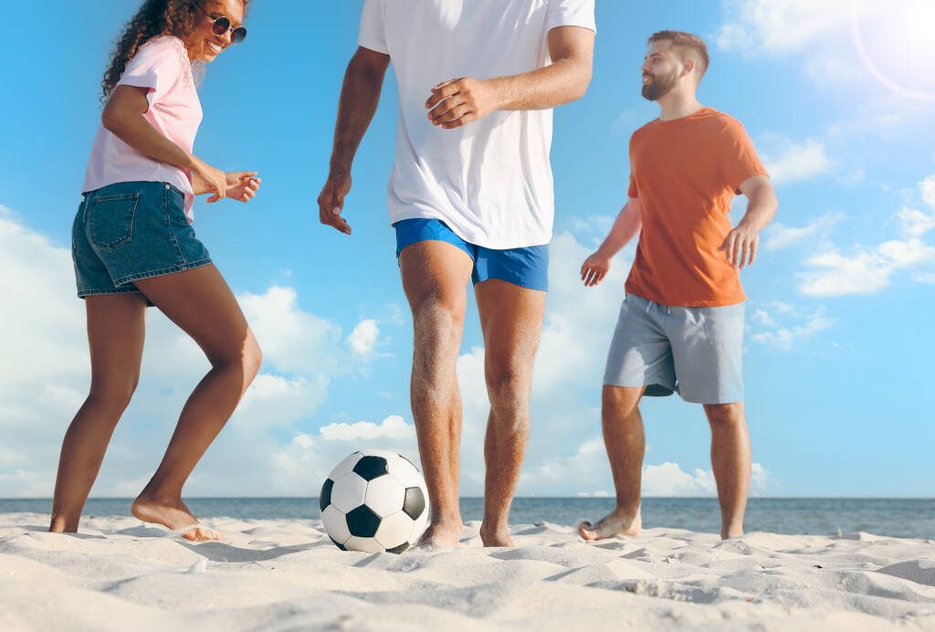 Onnelliset ystävät pelaavat jalkapalloa rannalla aurinkoisena päivänä, matala kulma näkymä - Valokuva, kuva