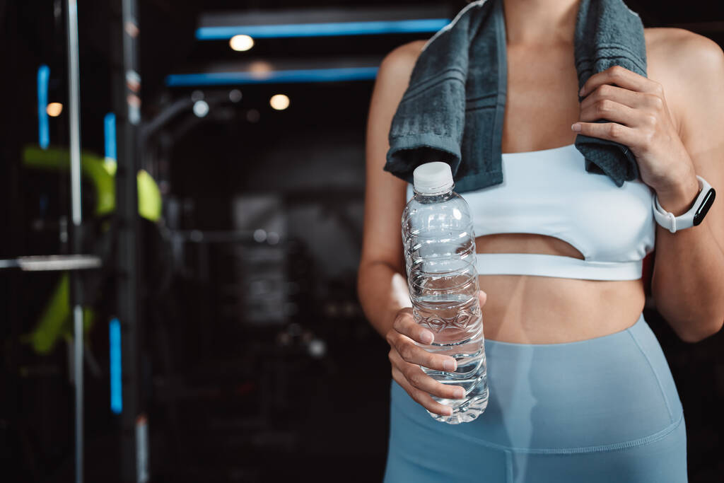 Vrouw drinkwater herstel gezondheid oefening training in fitnessruimte fitness breken ontspannen na het sporten met kettlebell, halters en waterfles gezonde levensstijl bodybuilding. - Foto, afbeelding