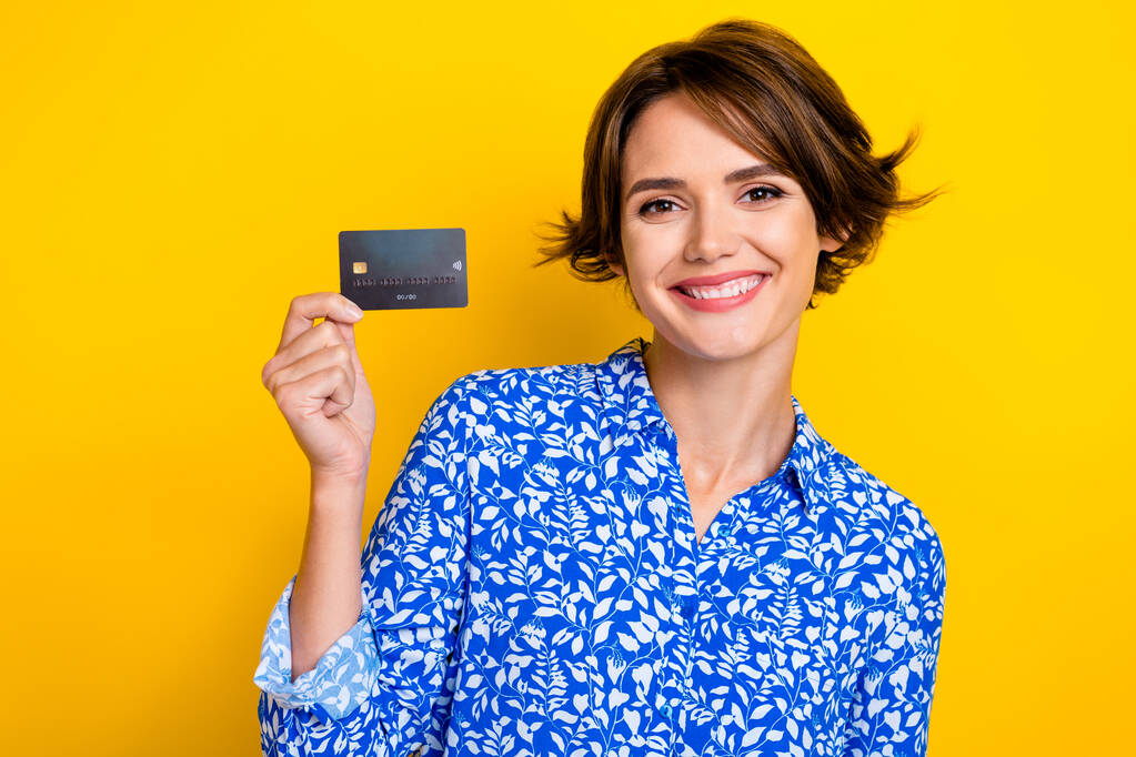 Φωτογραφία από θετική όμορφη κυρία φορούν μπλε κομψά ρούχα συστήσει τράπεζα πλαστική κάρτα απομονώνονται σε κίτρινο χρώμα φόντο. - Φωτογραφία, εικόνα