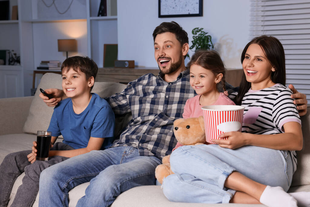 幸せな家族は夕方に自宅で映画を見ている。お父さんはリモコンでテレビチャンネルを変える - 写真・画像