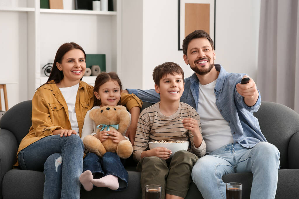 Ευτυχισμένη οικογένεια βλέποντας τηλεόραση στο σπίτι. Πατέρας αλλάζει κανάλια με τηλεχειριστήριο - Φωτογραφία, εικόνα