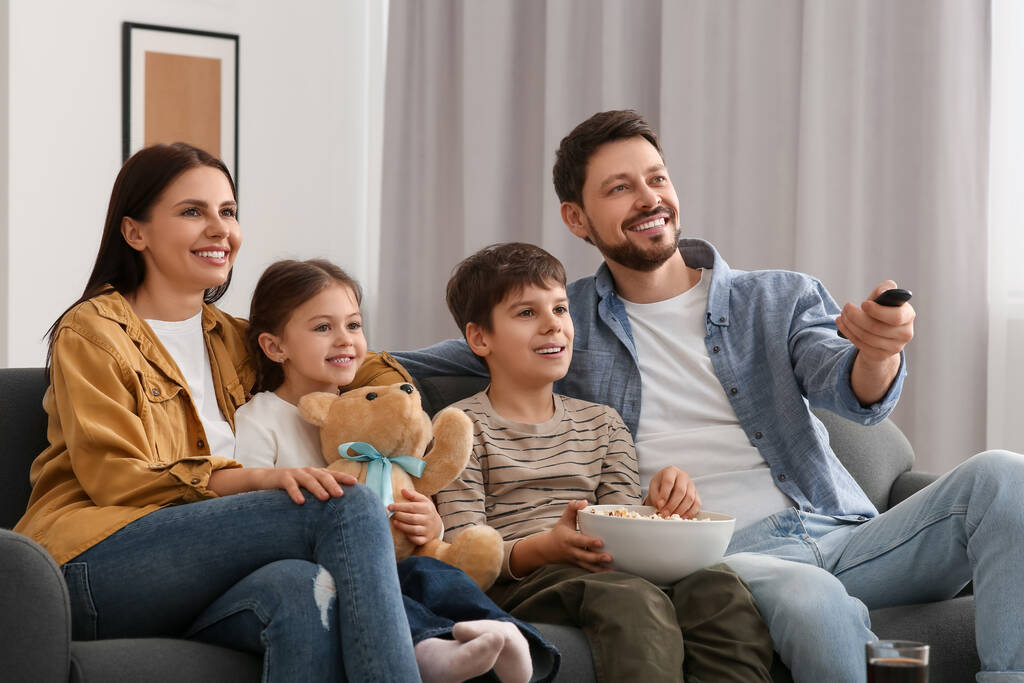 Šťastná rodina doma kouká na televizi. Otec přepíná kanály dálkovým ovládáním - Fotografie, Obrázek