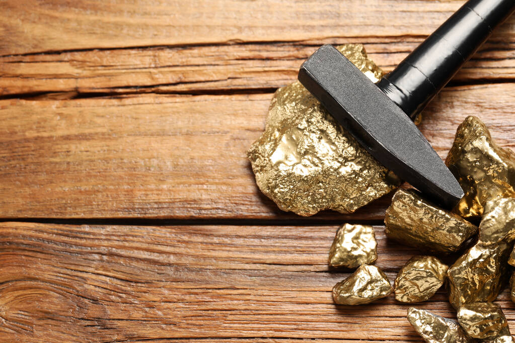 Pile of gold nuggets and hammer on wooden table, flat lay. Space for text - 写真・画像