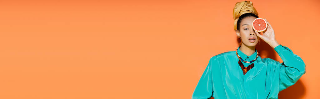 Donna afroamericana alla moda che tiene il pompelmo su sfondo arancione, banner  - Foto, immagini