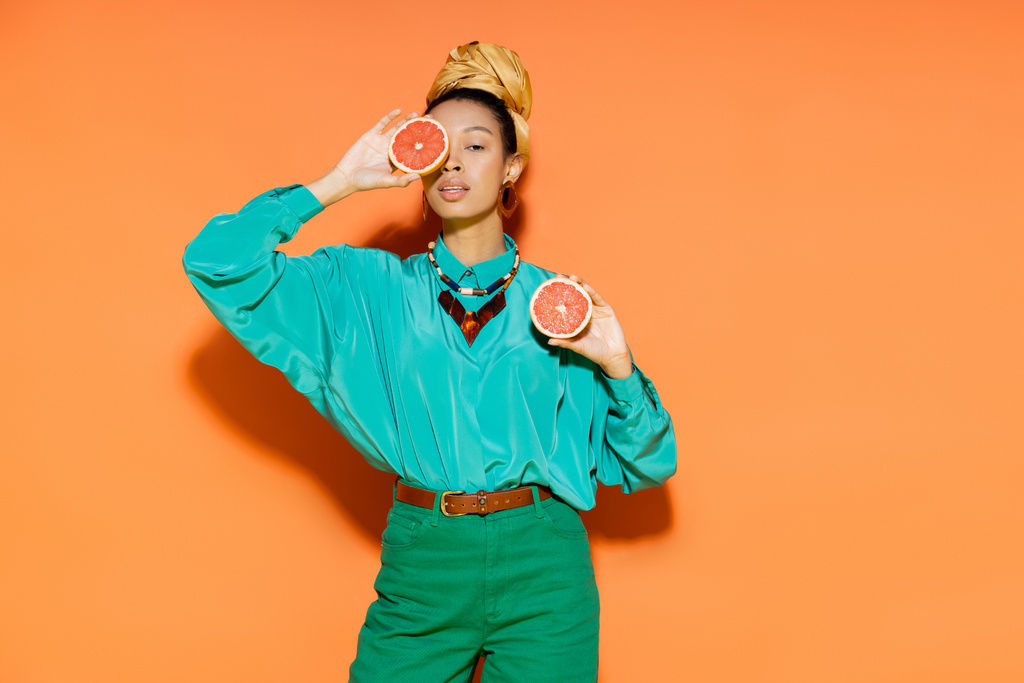Modelo americano africano na moda cobrindo rosto com toranja cortada no fundo laranja  - Foto, Imagem