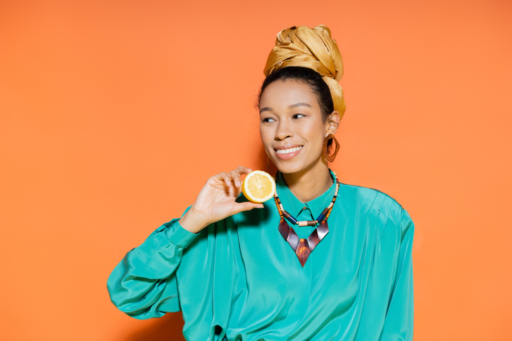 zorgeloos afrikaans amerikaans model in zomer outfit houden citroen op oranje achtergrond  - Foto, afbeelding