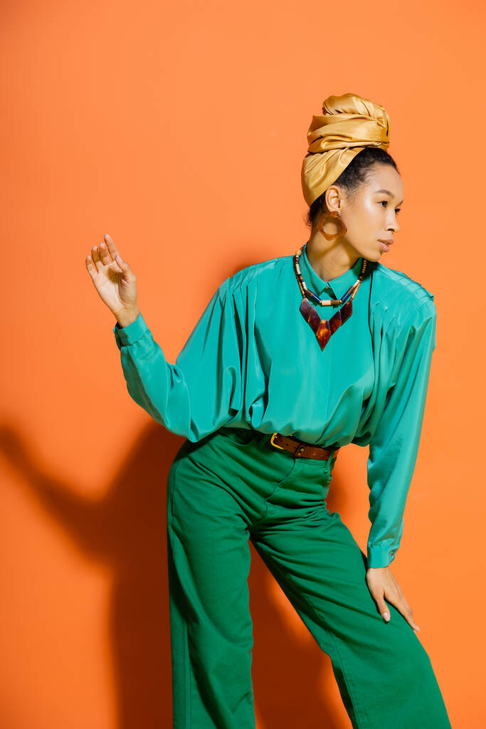Μοντέρνο αφρικανικό αμερικανικό μοντέλο σε φωτεινά ρούχα και κεφαλόδεσμο σε πορτοκαλί φόντο  - Φωτογραφία, εικόνα