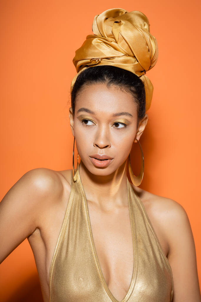 Trendy Afrikaans Amerikaans model in hoofddoek en badpak staand op oranje achtergrond  - Foto, afbeelding
