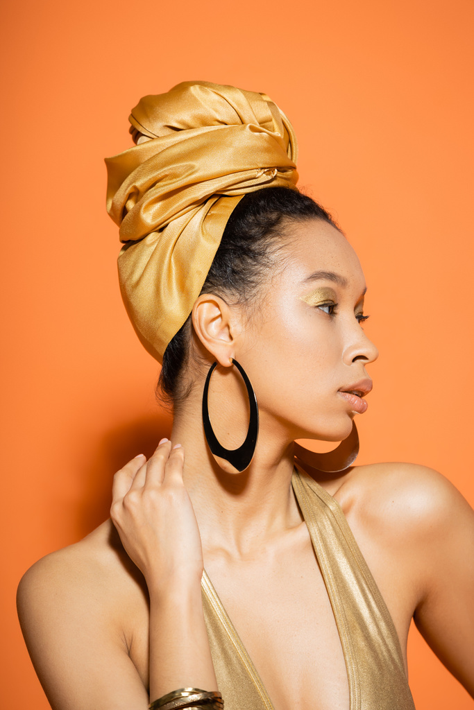 Retrato de afroamericano de moda en pañuelo dorado mirando hacia otro lado sobre fondo naranja  - Foto, imagen