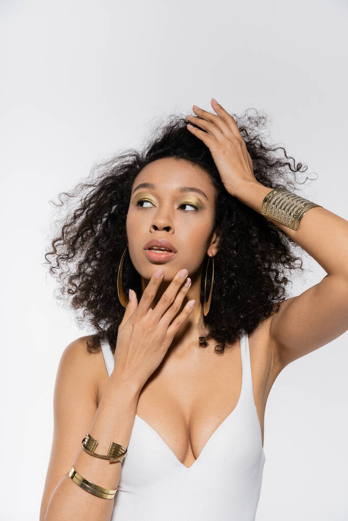 mladý africký americký model upravující kudrnaté vlasy a odvracející se izolované na šedé  - Fotografie, Obrázek