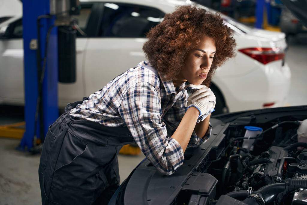 Zamyšlená žena automechanička kontroluje auto pod kapotou, auto je opravováno - Fotografie, Obrázek
