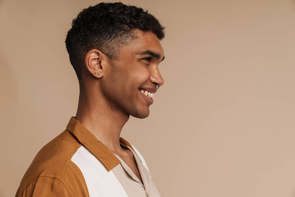 Retrato de perfil de un joven guapo y sonriente africano de pie sobre un fondo beige aislado - Foto, imagen