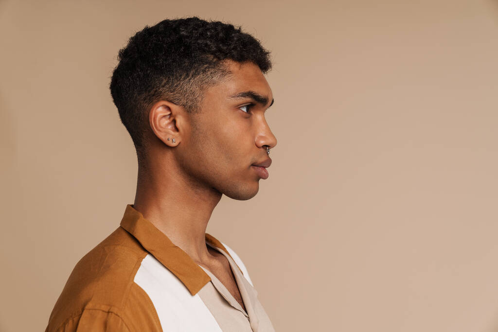 Profil portrait de jeune homme africain sérieux beau debout sur fond beige isolé - Photo, image