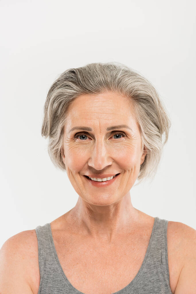 Porträt einer überglücklichen Seniorin, die in die Kamera lächelt und isoliert auf grau blickt  - Foto, Bild