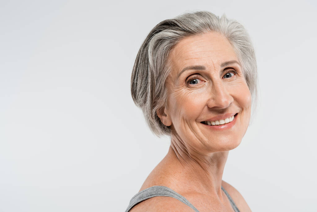 retrato de mujer mayor satisfecha con el pelo gris mirando a la cámara aislada en gris  - Foto, imagen