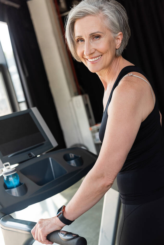 Glückliche Seniorin mit grauen Haaren trainiert auf Laufband im Fitnessstudio  - Foto, Bild