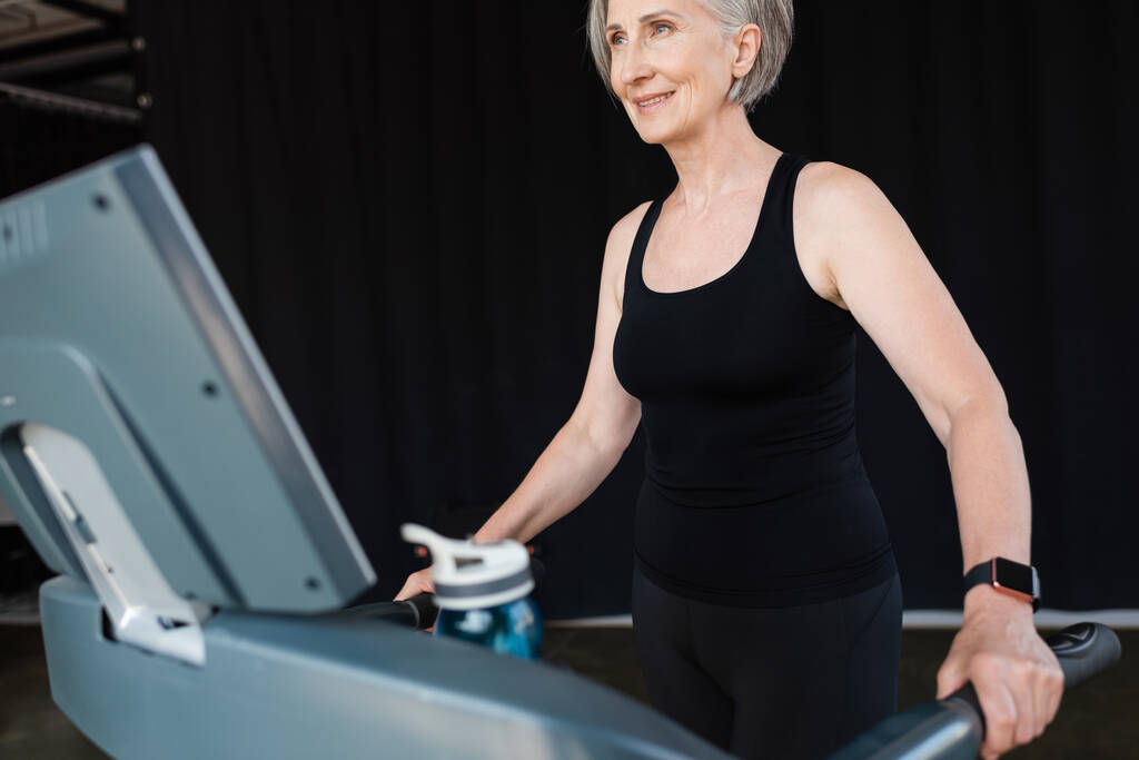 mulher sênior positivo com cabelos grisalhos trabalhando na esteira no ginásio   - Foto, Imagem