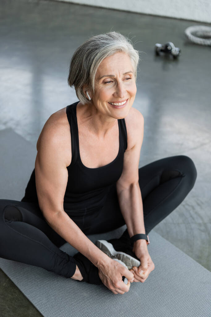 Blick aus der Vogelperspektive auf eine glückliche Seniorin, die auf der Fitnessmatte im Fitnessstudio lächelt  - Foto, Bild