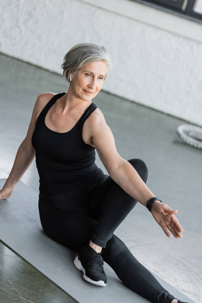longueur complète de la femme âgée en legging noir et débardeur exercice sur tapis de fitness dans la salle de gym  - Photo, image