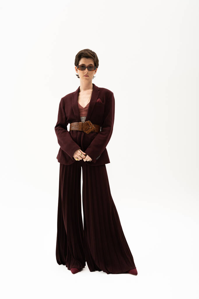 longitud completa de la mujer elegante en pantalones de palazzo y chaqueta marrón con cinturón de cuero sobre fondo blanco - Foto, imagen